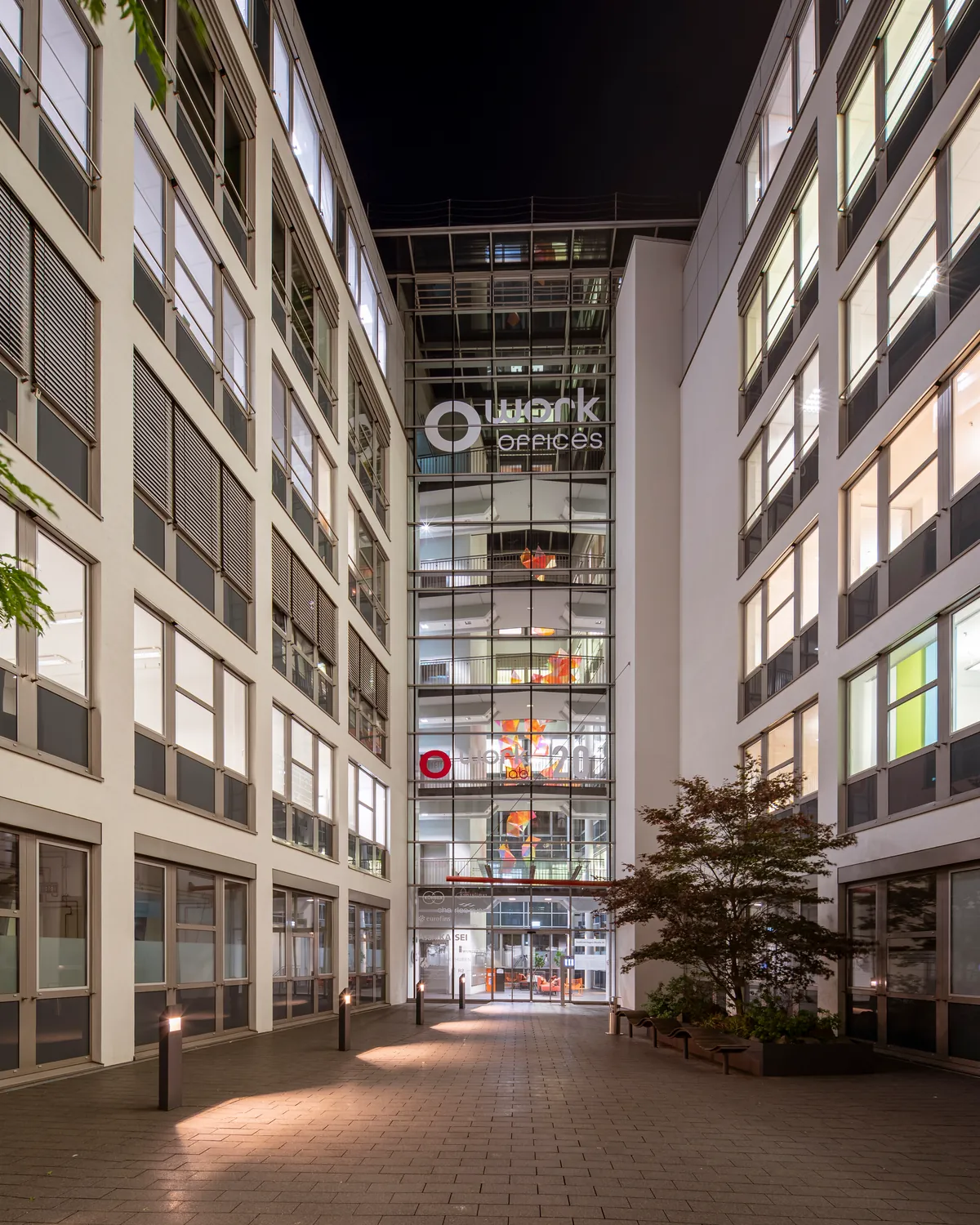 Beleuchteter Innenhof mit Glasatrium und Eingangsbereich eines Bürokomplexes in Köln-Kalk – Objekt der Unterhaltsreinigung durch Gebäudereinigung Wunderlich
